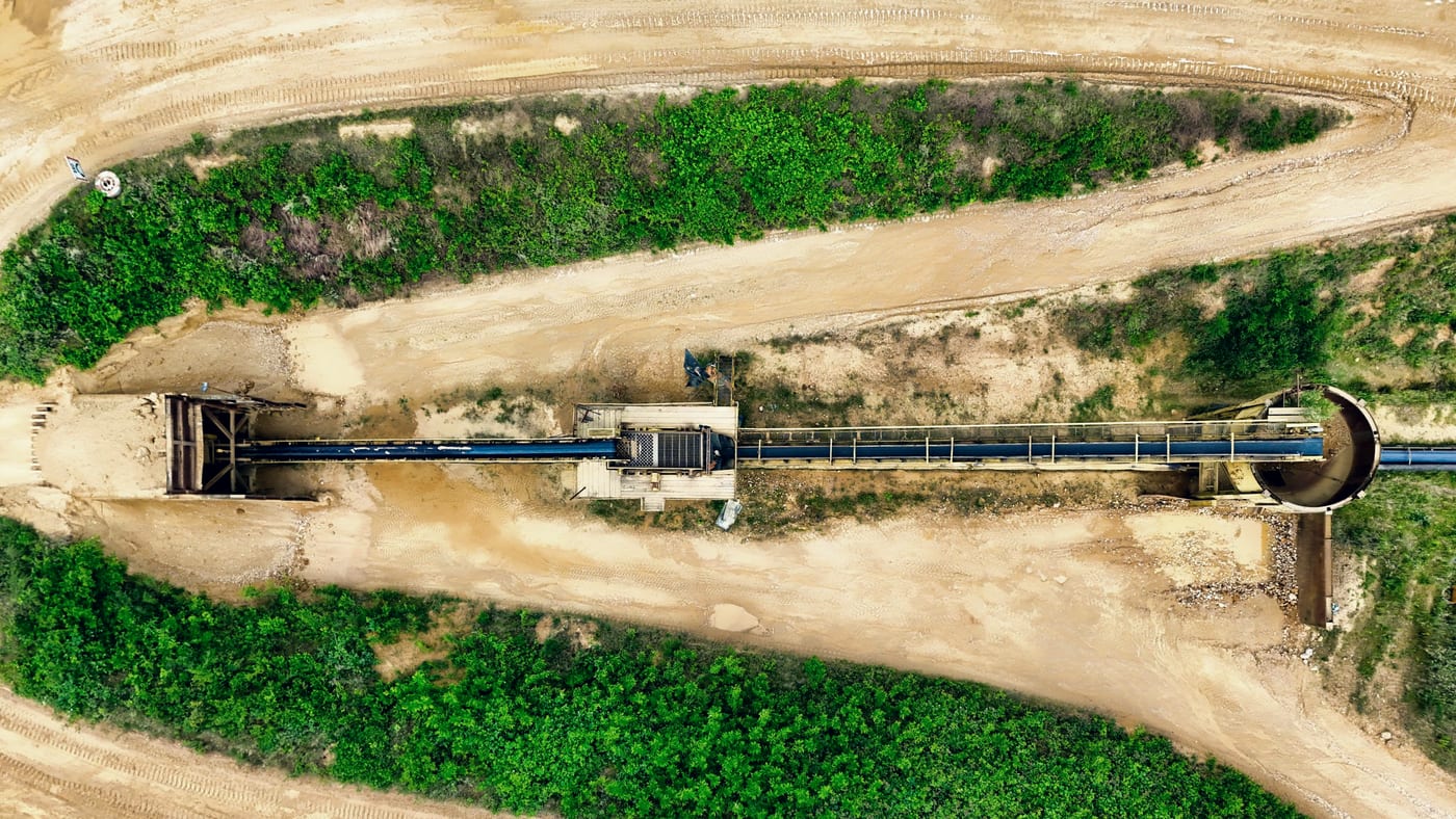 Overhead view of a conveyor running between haul roads at a materials handling operation.