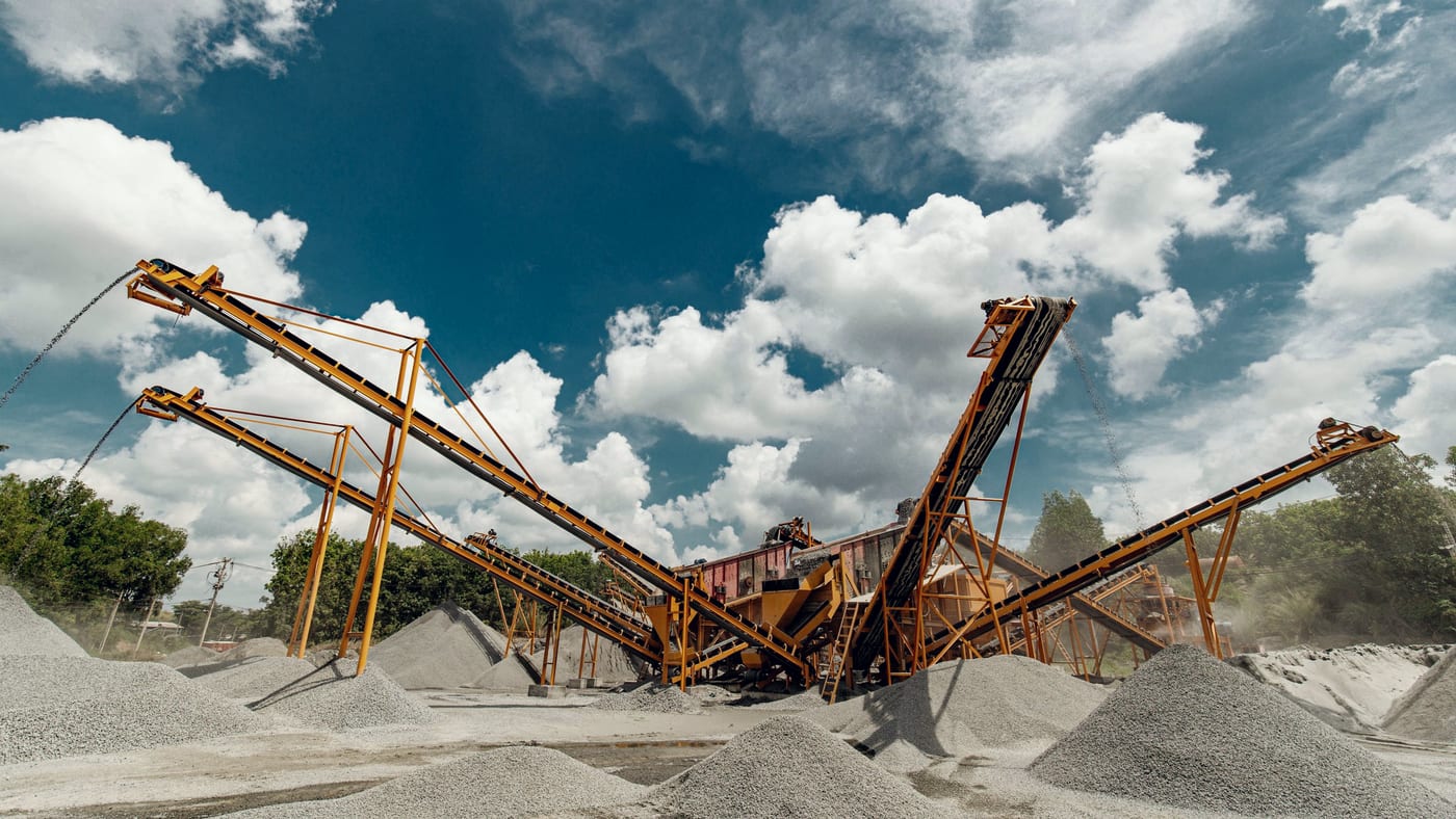 A screening and conveyor plant stacking processed aggregate, structures silhouetted against a cloudy sky.