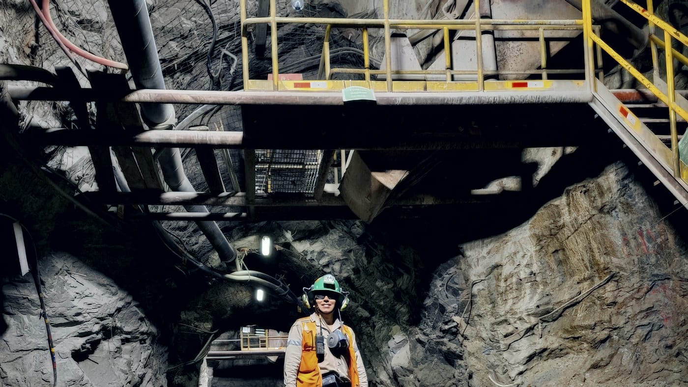 An engineer in high-visibility clothing and hard hat walking a wet underground mine drive, services running overhead.