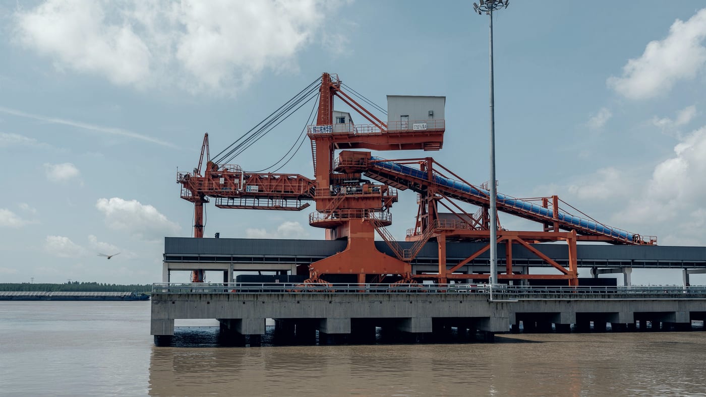 A bulk loading gantry on a river wharf, seen from the water, with no vessel alongside.